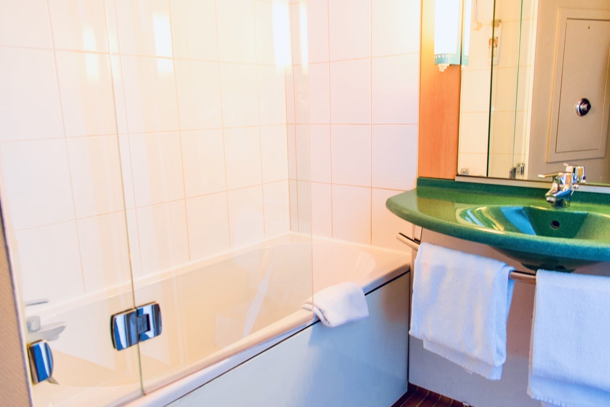Un baño con una bañera, un lavamanos verde y un espejo.