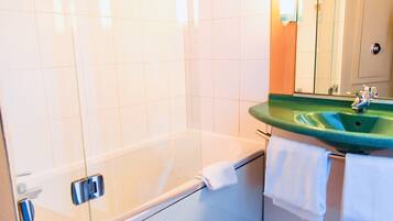 Un baño con una bañera, un lavamanos verde y un espejo.