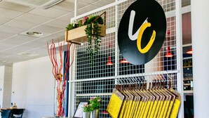 Et moderne interiør med en væg af metalgitter, en hængende plante, en vase med røde sløjfer og et rundt skilt med et gult 'C'.