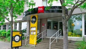 En hotelindgang med en trappe, der fører op til døren, et skilt og et træ i forgrunden.