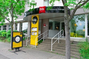 Een hotelingang met een trap die naar de deur leidt, een naambord en een boom op de voorgrond.