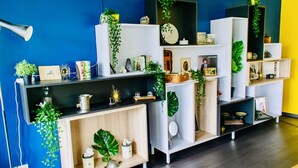 Et moderne værelse med blå væg, træhylder og forskellige dekorative elementer, heriblandt planter og billeder i rammer.