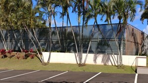 A fenced parking area with a clear sky and palm trees. - Banyan Harbor Resort (Lihue)