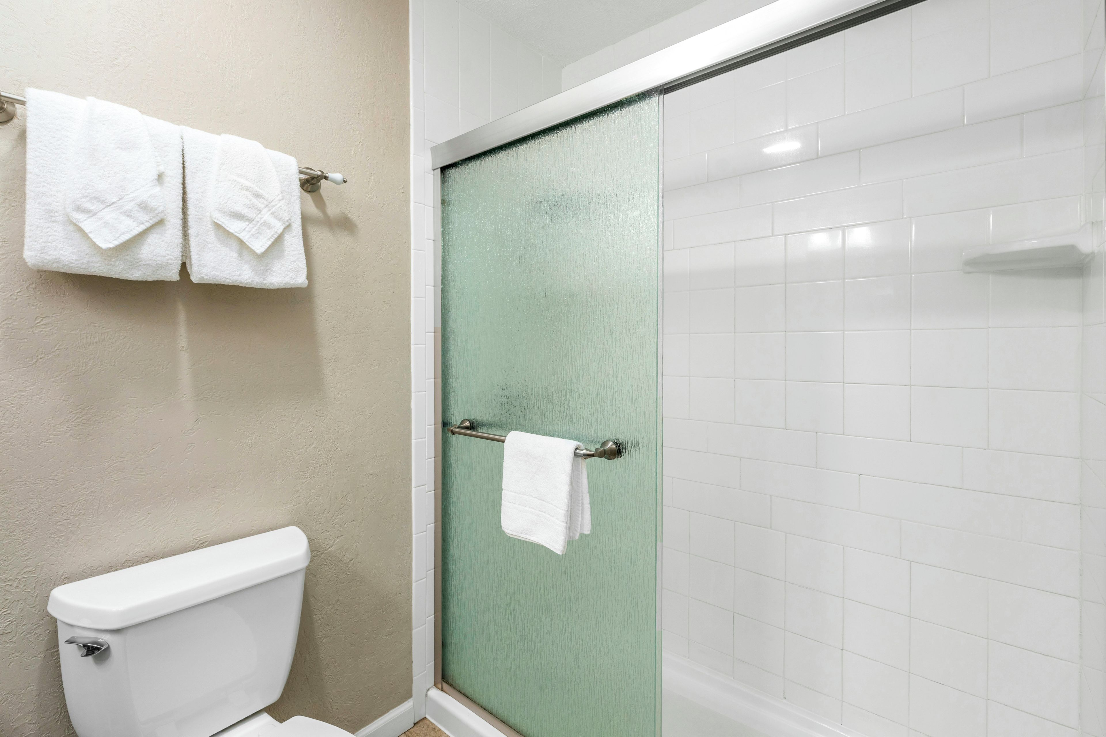 A bathroom with a toilet, a glass shower door, and a towel rack with two towels.