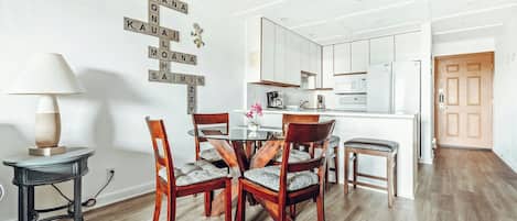 A dining area with a round table, four chairs, a lamp, and a wall with a Scrabble game.