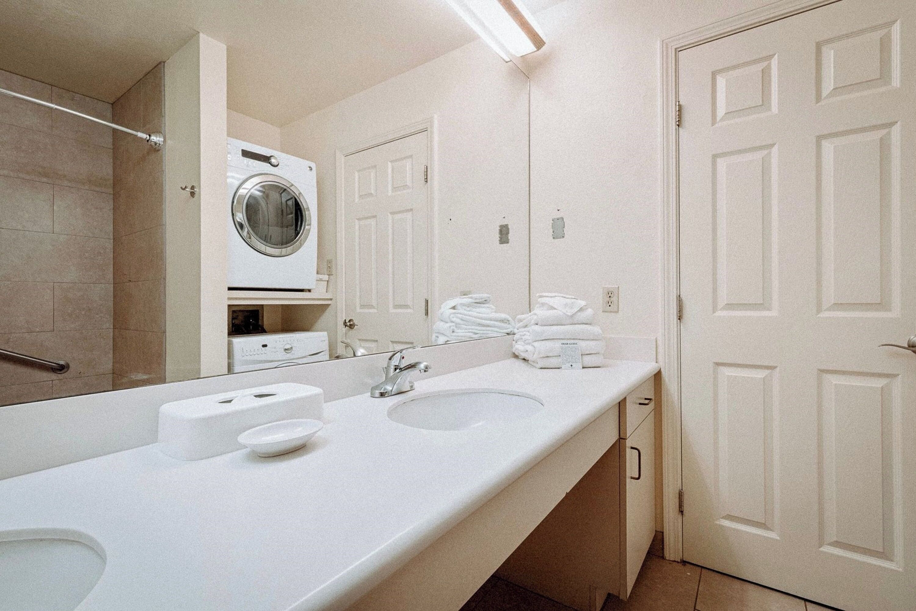 Un baño de hotel con lavamanos doble, un espejo, lavadora y un tendedero.