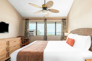 A hotel room with a bed, a television, a ceiling fan, a window with curtains, and a view of the outdoors. - Banyan Harbor Resort (Lihue)