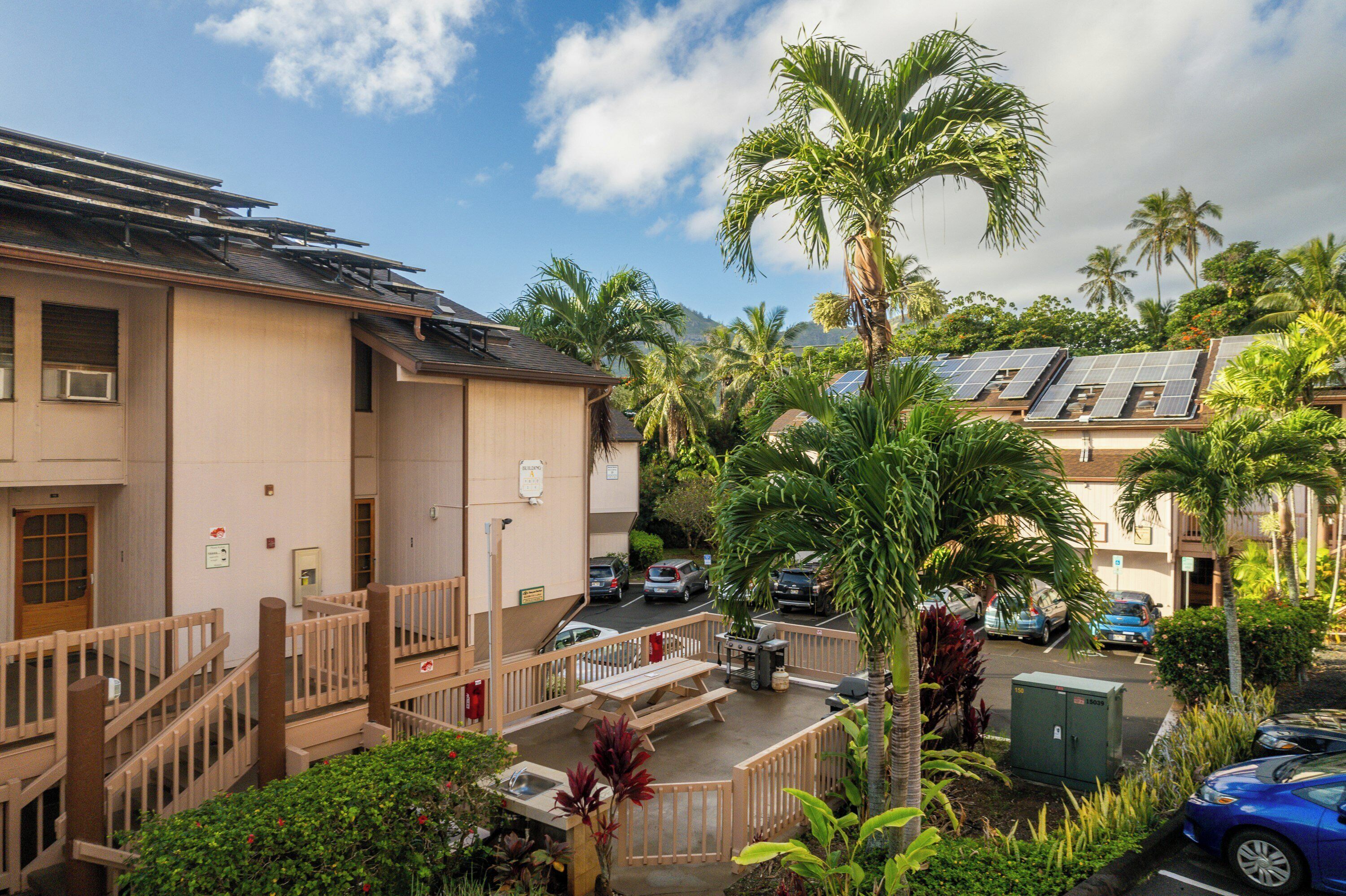 A residential building with solar panels, a covered parking area, and a view of palm trees.