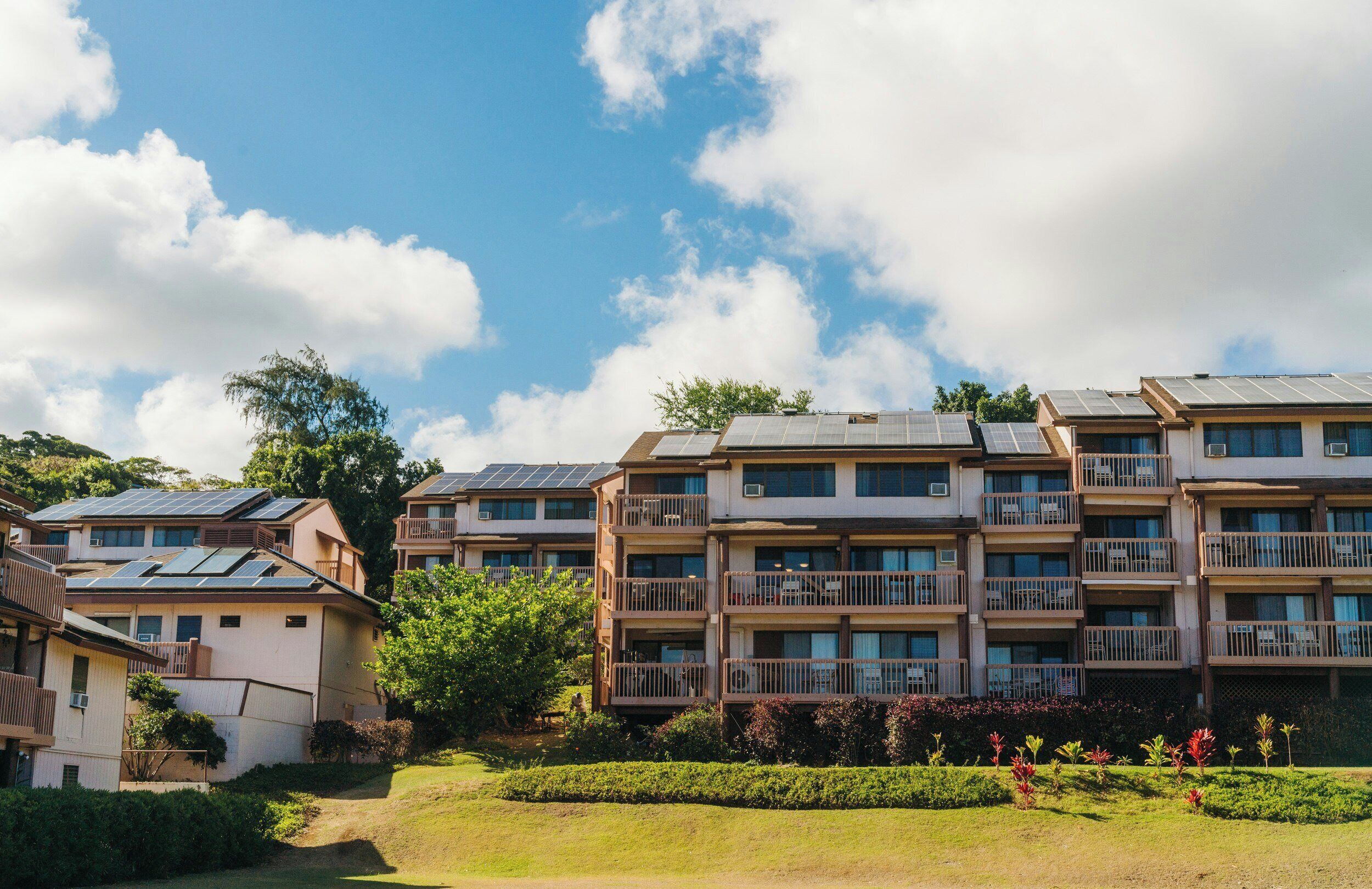 Un edificio residencial de varios pisos con paneles solares en el techo, rodeado de vegetación y un cielo despejado.