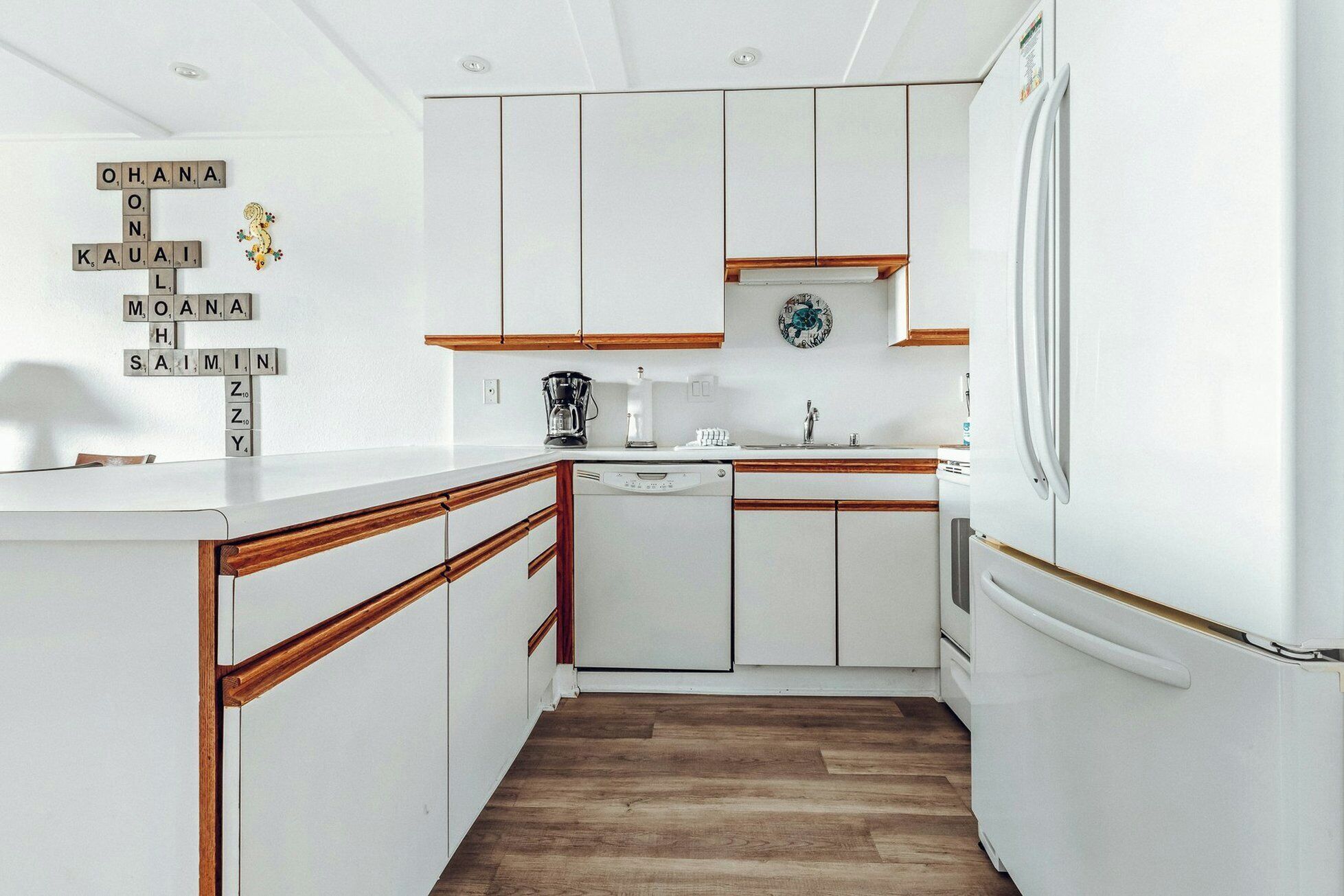 A kitchen with white cabinets, wooden countertops, a coffee maker, and a clock on the wall.