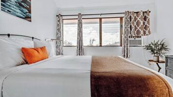 A hotel room with a bed, a window with curtains, a plant, and a radiator.