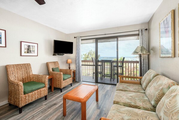 A living room with wicker furniture, a flat-screen TV, and a balcony with a view. - Banyan Harbor Resort (Lihue)