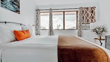 Una habitación con cama, ventana con cortinas, una planta y un equipo de aire acondicionado.