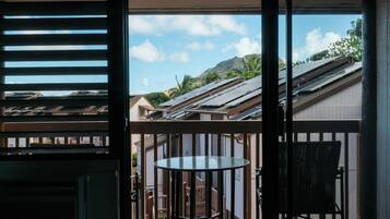Ein Balkon mit Tisch und Stuhl, Blick auf Nachbarhäuser und ein Berg in der Ferne.