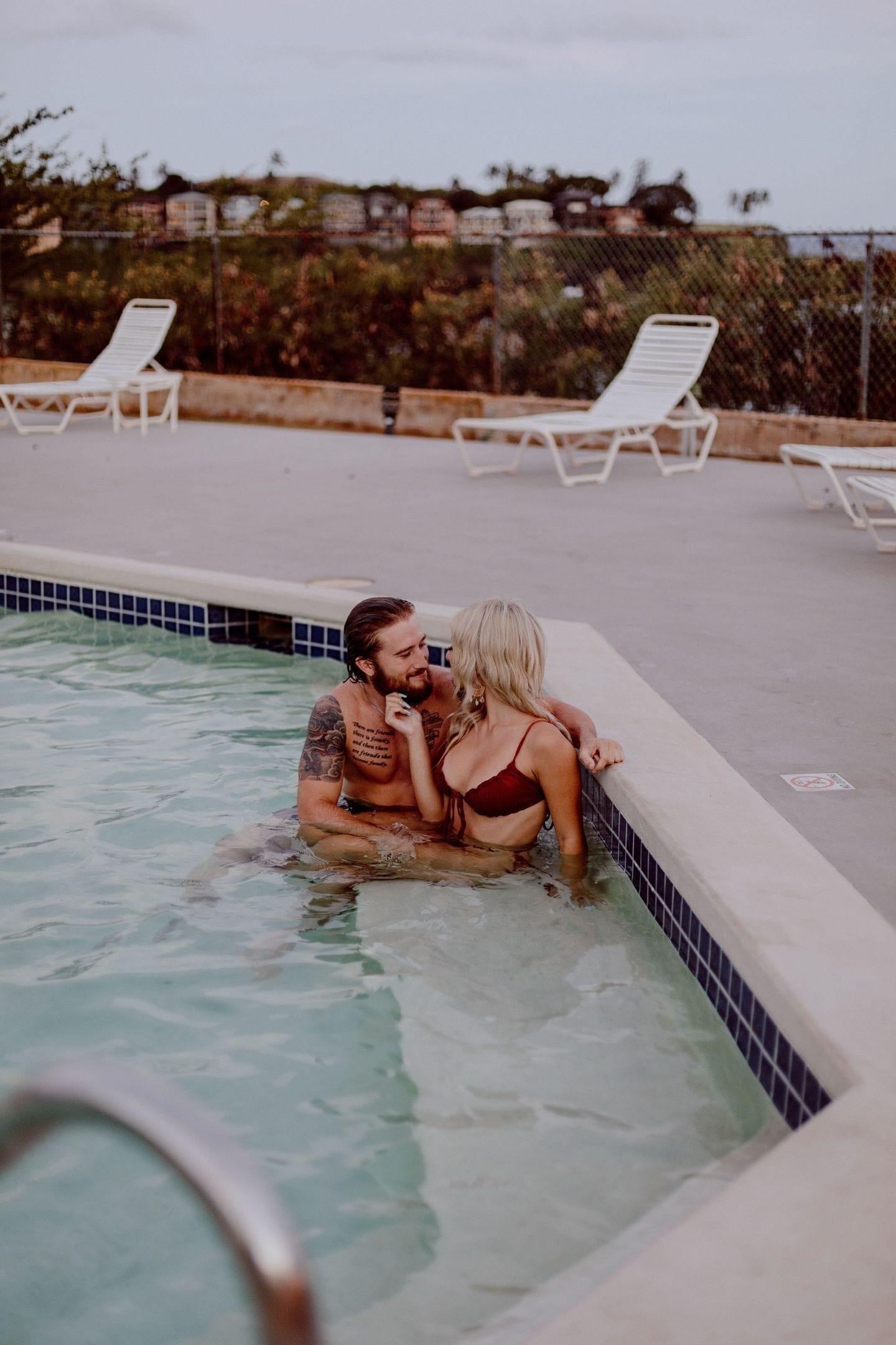 Una piscina con sillas de descanso y una valla al fondo.