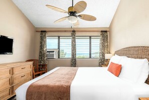 Habitación de hotel con cama, ventilador de techo, televisor, ventana con cortinas y unidad de aire acondicionado.