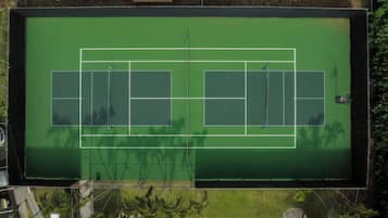 Vista aérea de una cancha de tenis con dos pistas, rodeadas de vegetación y paneles solares.