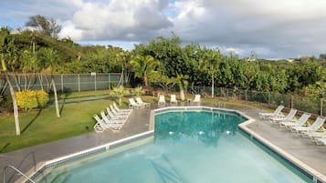 A swimming pool with lounge chairs and a grassy area with trees.
