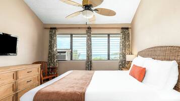 A hotel room with a bed, a television, a ceiling fan, a window with curtains, and a view of the outdoors.