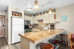 A kitchen with a central island, stainless steel appliances, and wooden bar stools. - Banyan Harbor Resort (Lihue)