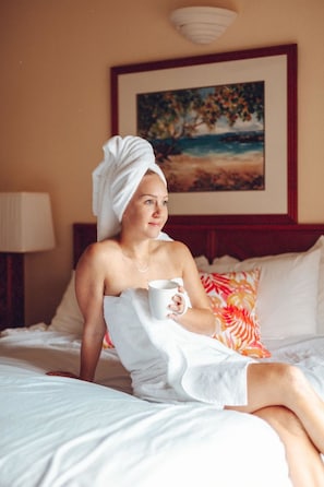 A person sitting on a bed with a towel wrapped around their head, holding a mug. - Banyan Harbor Resort (Lihue)