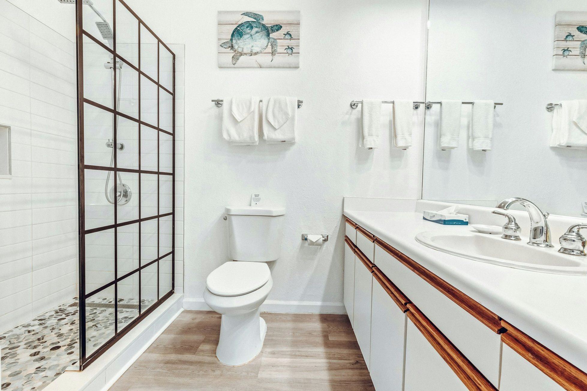 Een moderne badkamer met een glazen douchecabine, toilet, wastafel met spiegel en meerdere handdoekhaken.