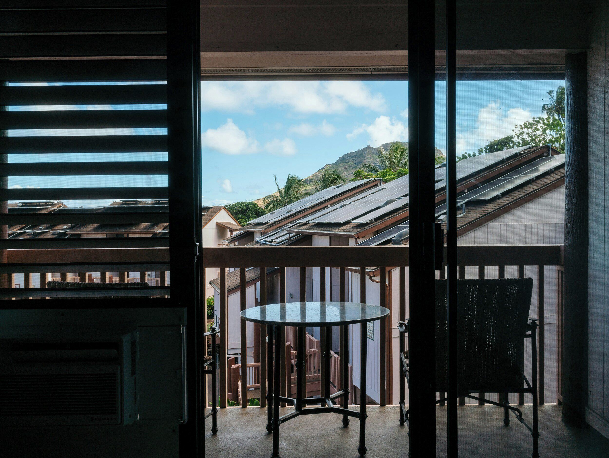 Un balcon avec une table et une chaise, une vue sur les maisons voisines et une montagne à l’horizon.