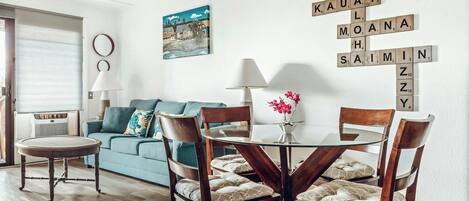 A living room with a blue sofa, a round table with chairs, and a wall with Scrabble tiles spelling out words.