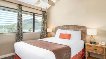 A hotel room with a bed, two bedside tables, a nightstand, a ceiling fan, and a window with curtains.