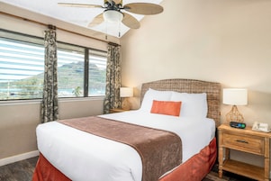 Habitación de hotel con cama, dos mesitas de noche, un velador, un ventilador de techo y una ventana con cortinas.