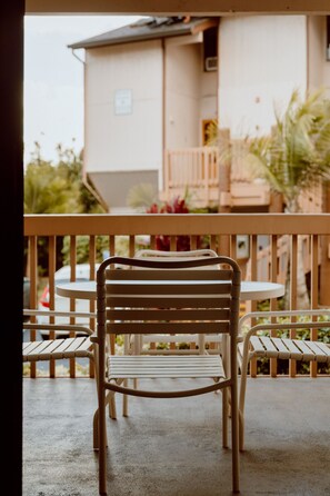 A balcony with a metal chair and a small table, a building in the background, and some greenery. - Banyan Harbor Resort (Lihue)