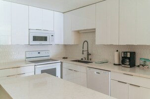 Una cocina moderna con armarios blancos, microondas integrado, pileta de acero inoxidable y cafetera.