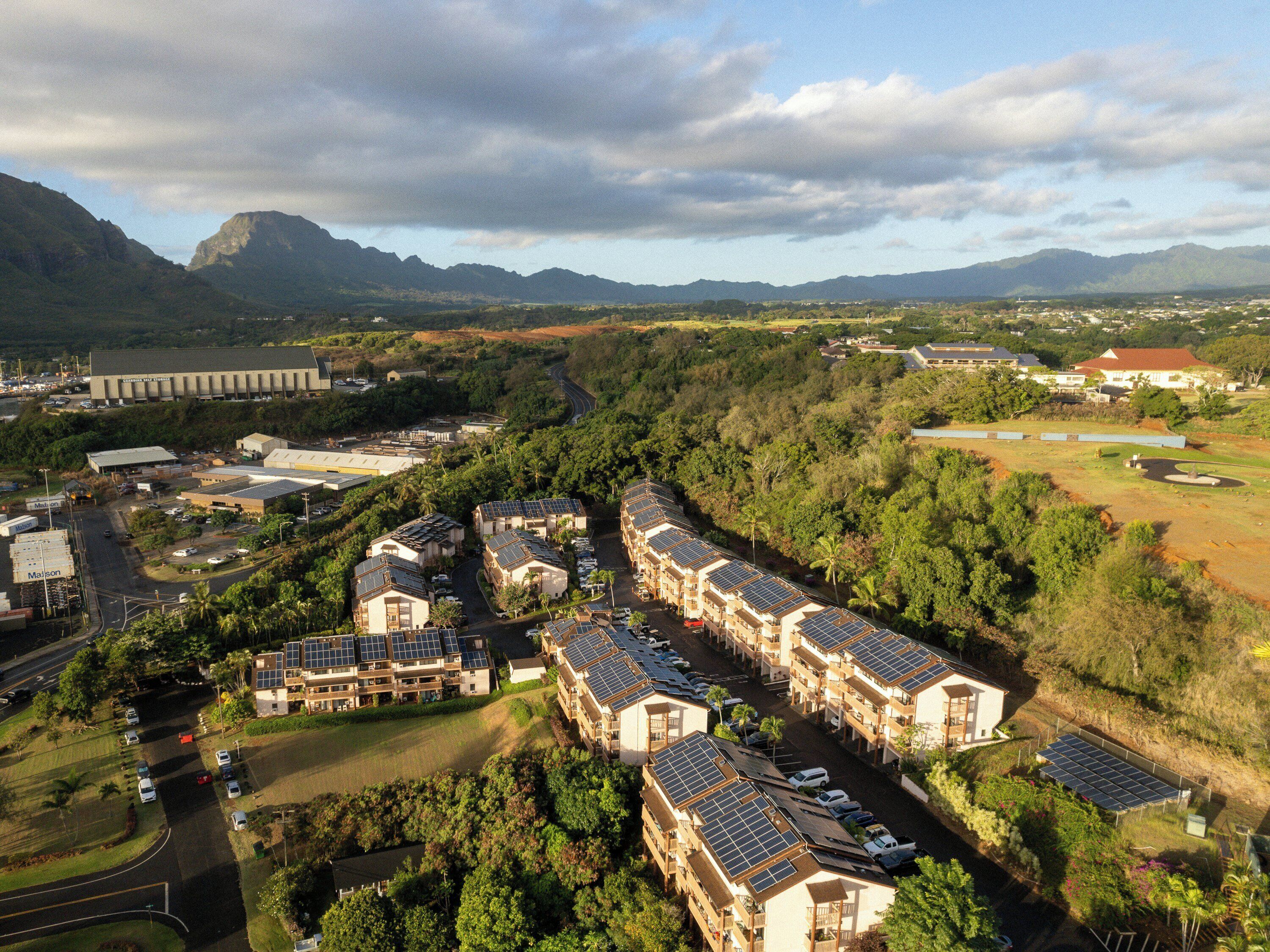 A residential area with multiple buildings, roads, and a large industrial facility in the background.