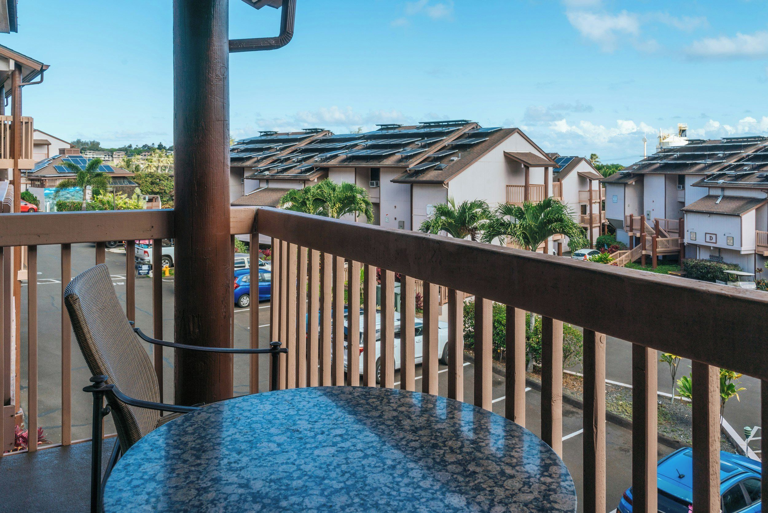 A balcony with a round table and a chair, overlooking a street with multiple houses and parked cars.