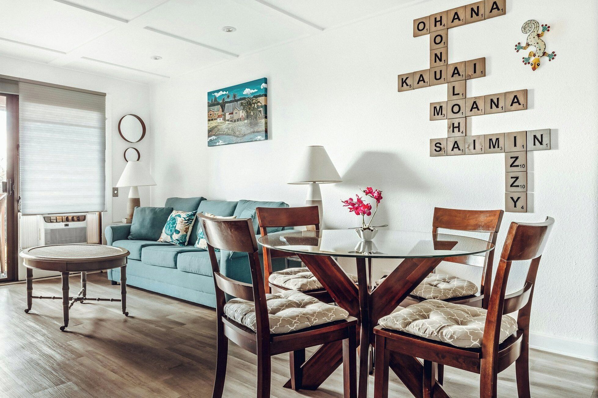 A living room with a blue sofa, a round table with chairs, and a wall with Scrabble tiles spelling out words.