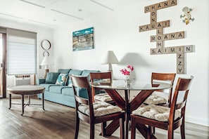 A living room with a blue sofa, a round table with chairs, and a wall with Scrabble tiles spelling out words. - Banyan Harbor Resort (Lihue)
