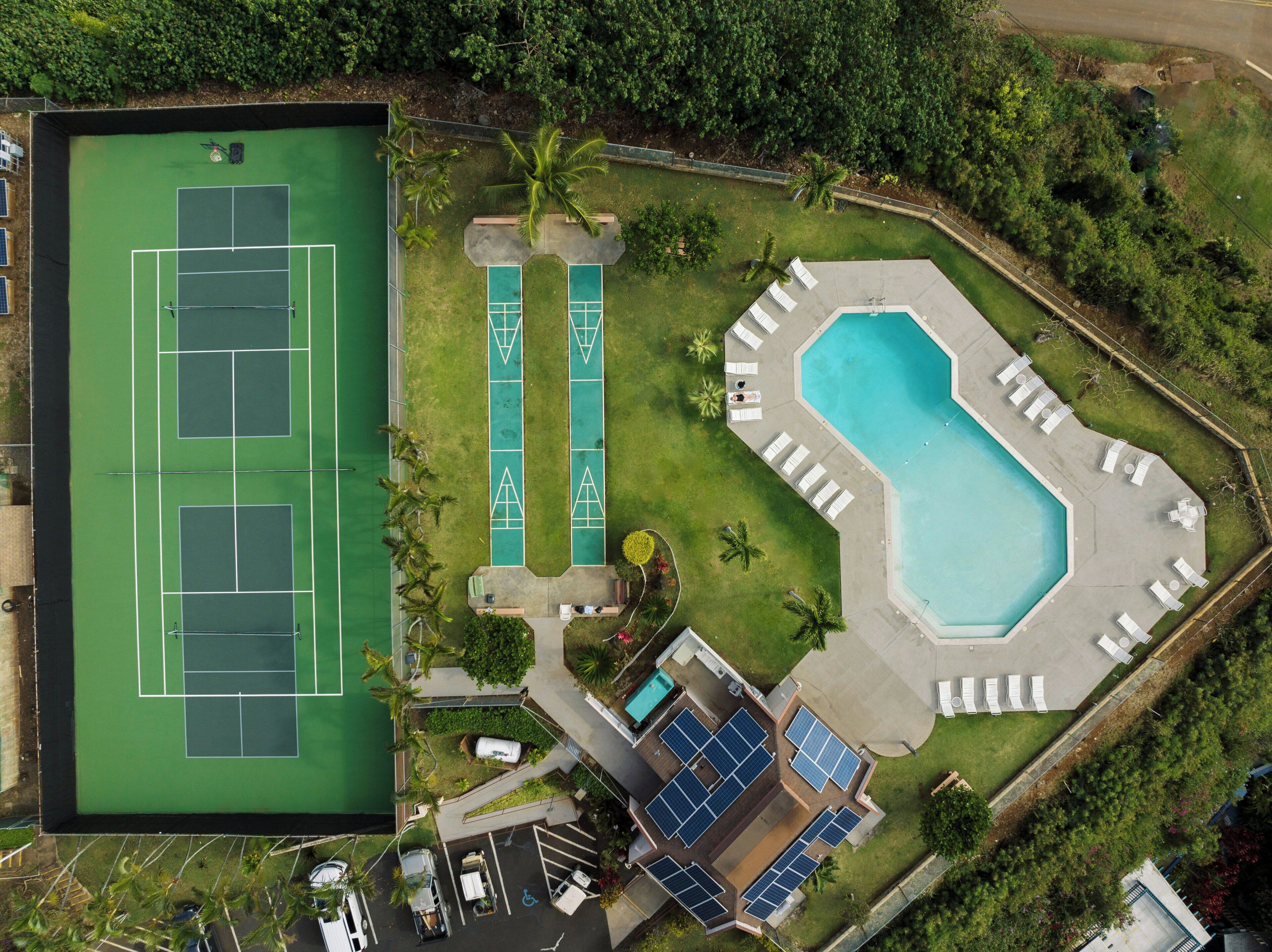 An aerial view of a property with a tennis court, a swimming pool, and solar panels.
