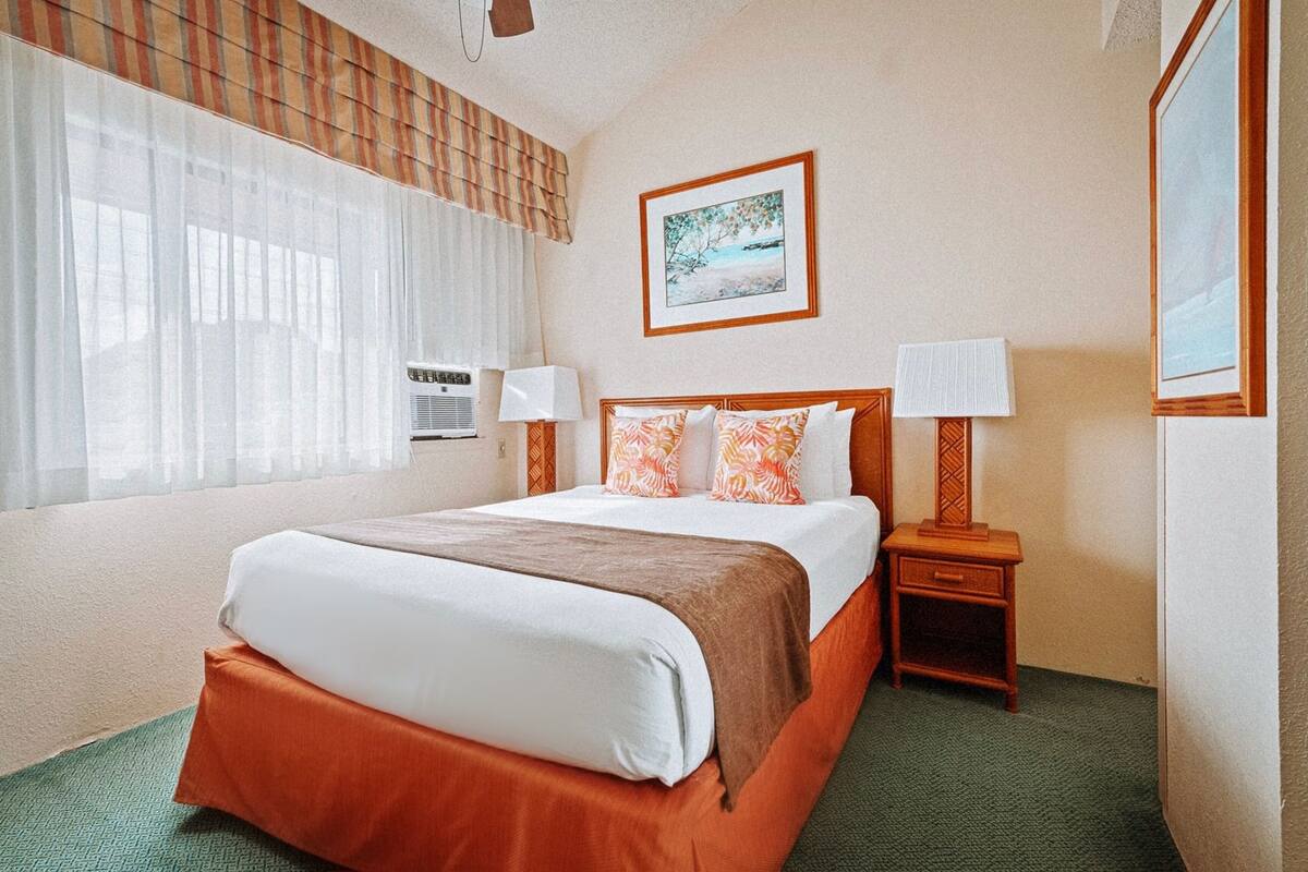 A hotel room with a large bed, two bedside tables, a window with curtains, and a painting on the wall.