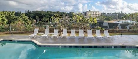 A swimming pool with lounge chairs and a view of a beach and buildings in the background.