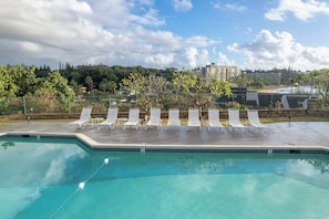 A swimming pool with lounge chairs and a view of a beach and buildings in the background. - Banyan Harbor Resort (Lihue)