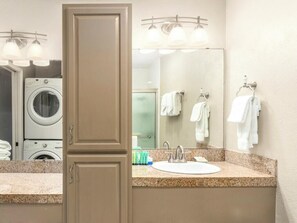 A hotel bathroom with a sink, mirror, towel rack, and washing machine. - Banyan Harbor Resort (Lihue)