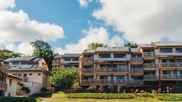 Un immeuble résidentiel à plusieurs étages, doté de panneaux solaires sur le toit, entouré de verdure et surplombant un ciel dégagé.