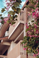 Un edificio de varios pisos con balcones y un árbol con flores rosadas al frente.