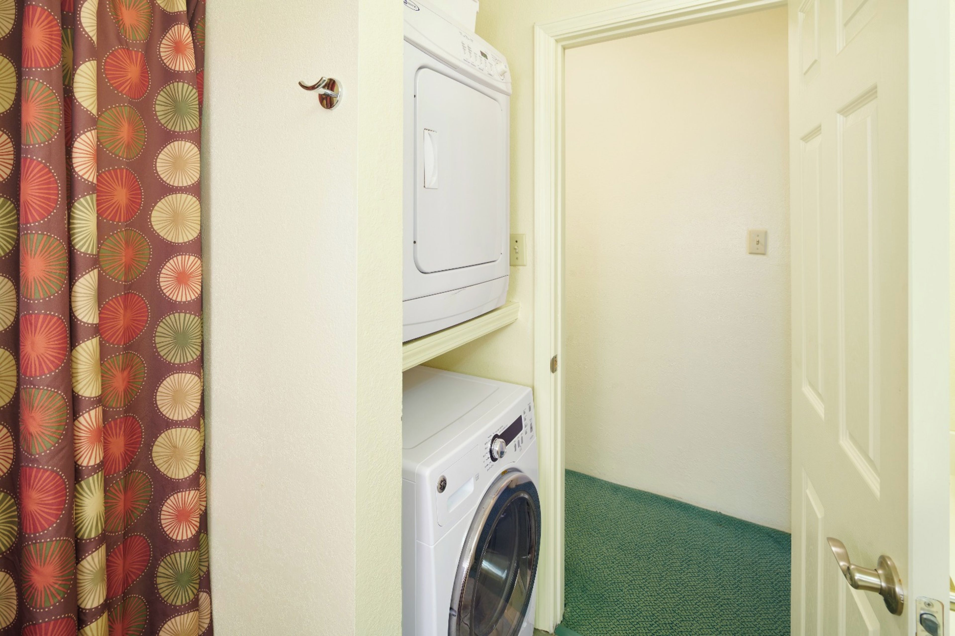 A laundry room with a washing machine and dryer, a door, and a patterned curtain.