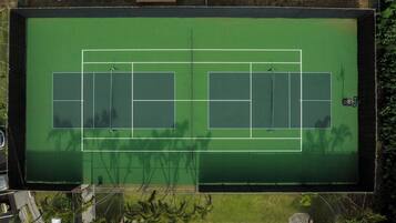 An aerial view of a tennis court with two courts, surrounded by greenery and solar panels.