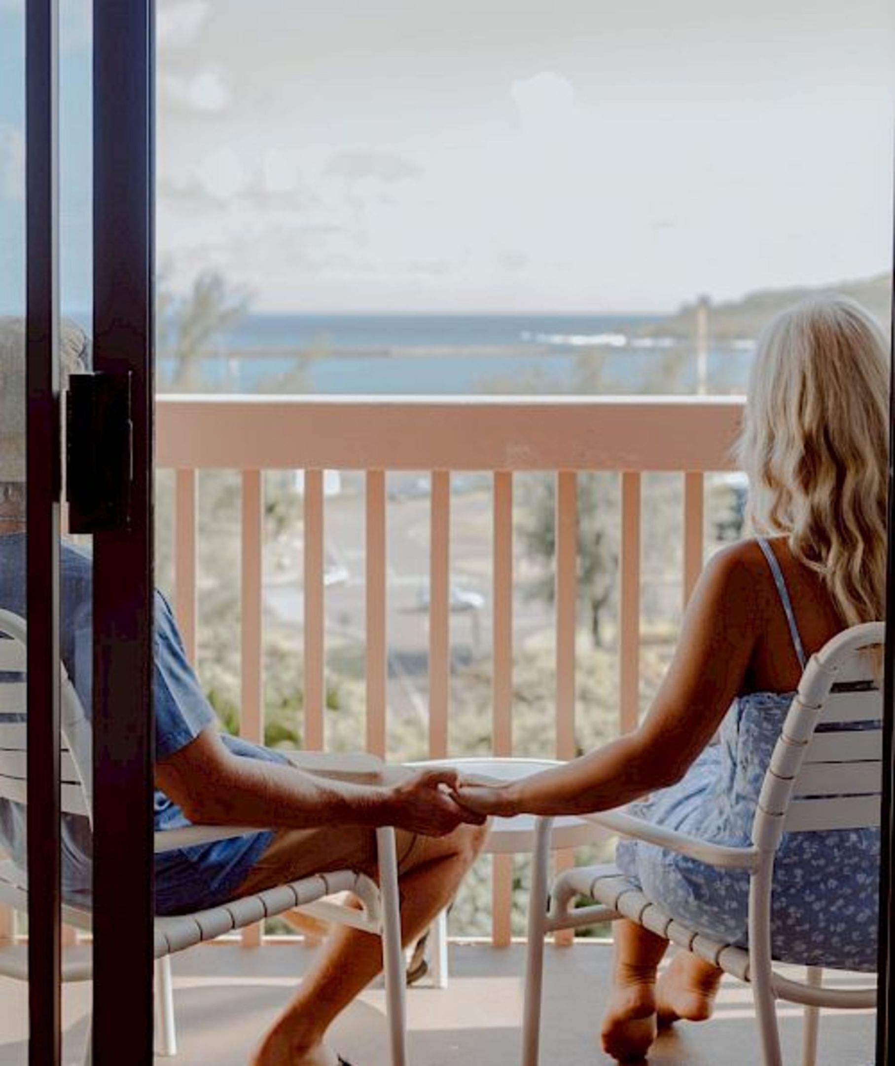A balcony with a view of the ocean, a person in a blue shirt, and another in a floral dress.