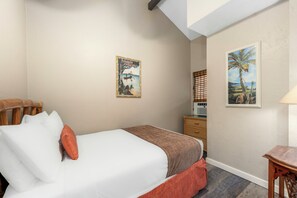 A hotel room with a bed, a wooden headboard, a nightstand, a lamp, and two wall art pieces.