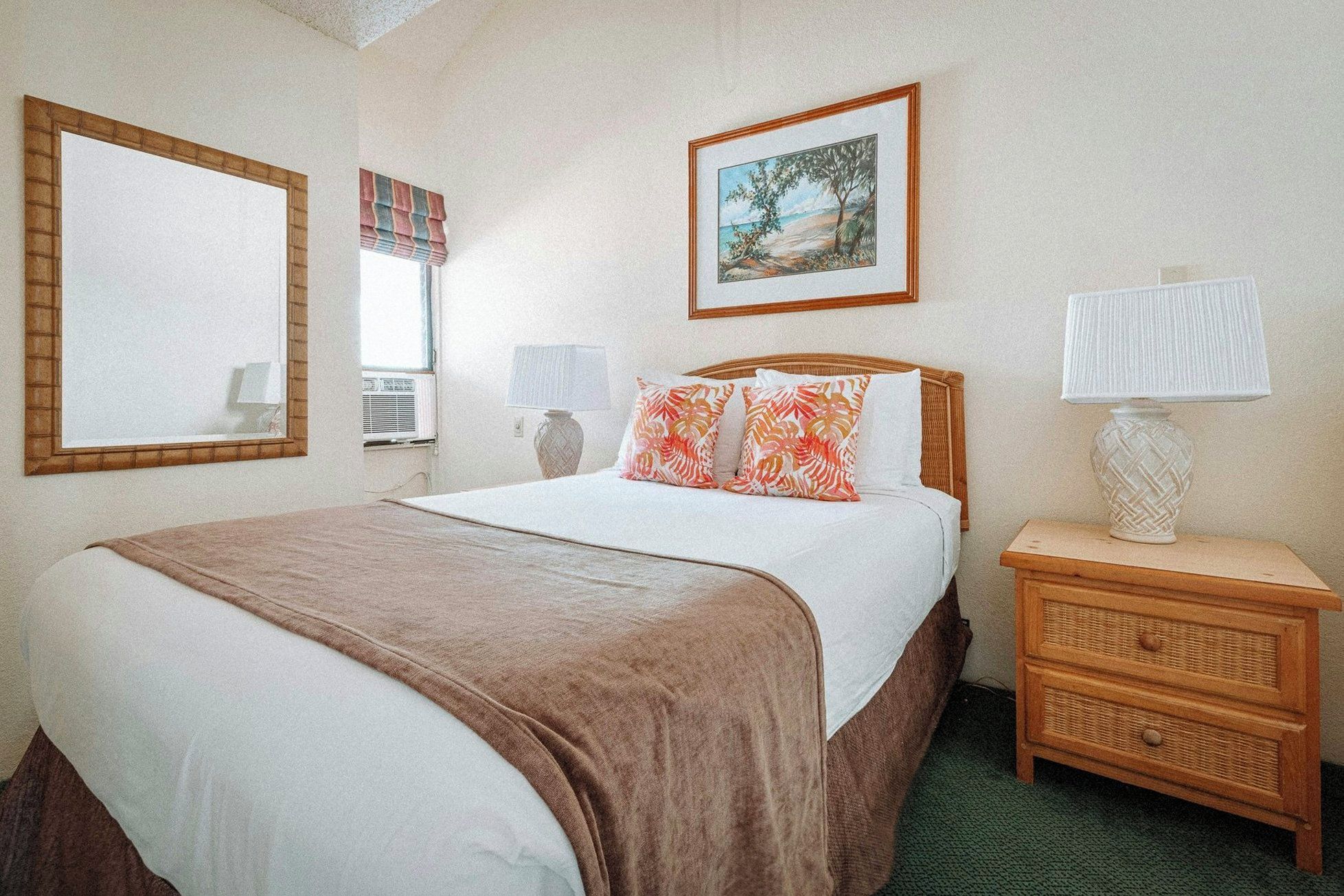 A hotel room with a bed, a nightstand, a lamp, a framed picture on the wall, and a window with blinds.