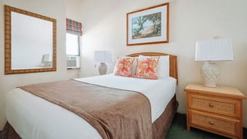 A hotel room with a bed, a nightstand, a lamp, a framed picture on the wall, and a window with blinds.