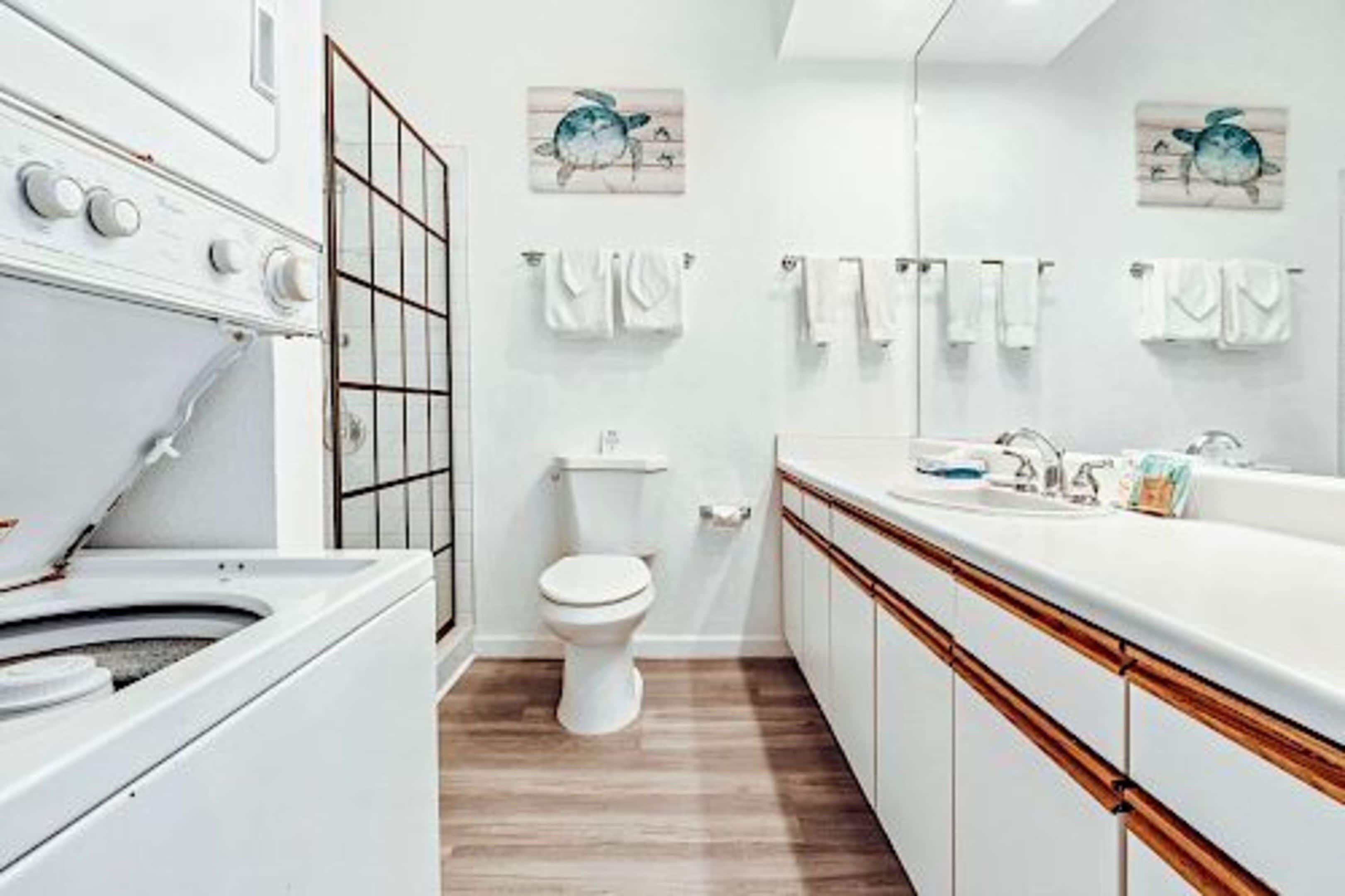 Un baño moderno con lavamanos, inodoro y un espejo grande. Hay dos toallas colgadas en la pared y un armario de madera.